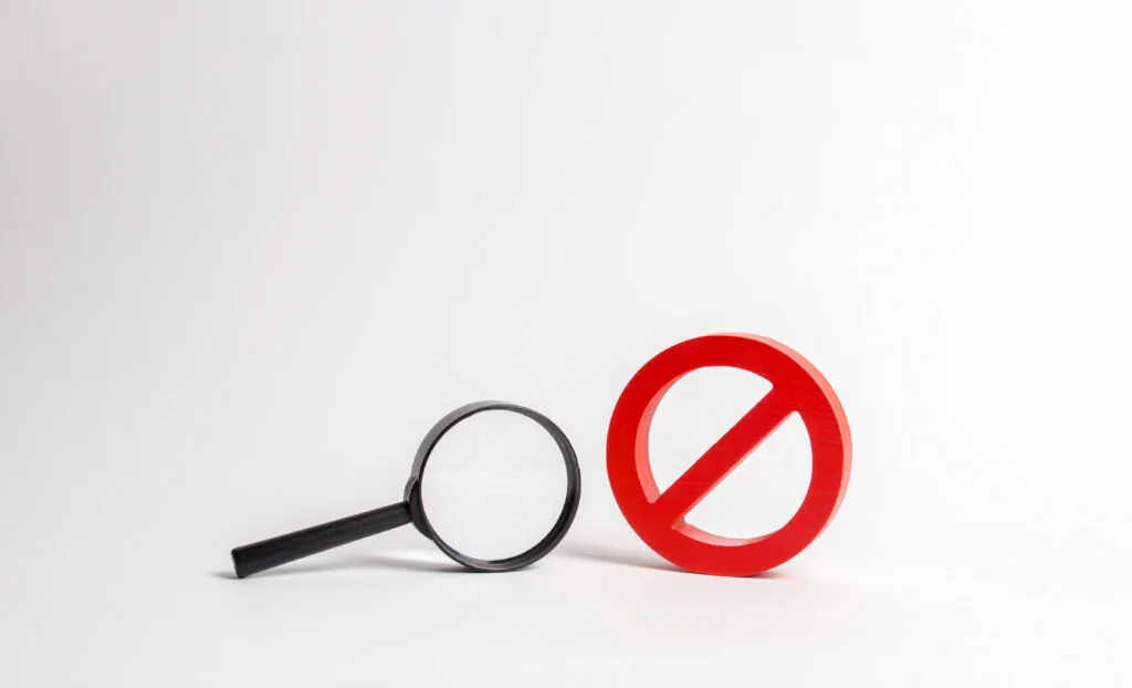 Loupe à côté d’un panneau d’interdiction rouge.
