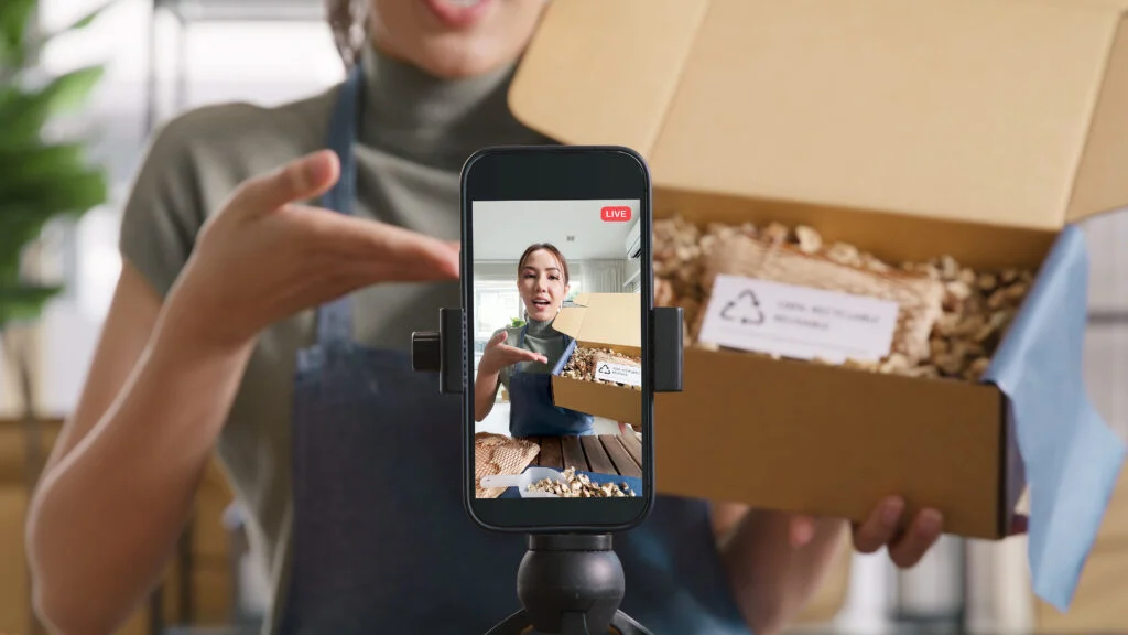 Créatrice filmant la présentation d’un colis avec un smartphone sur trépied.