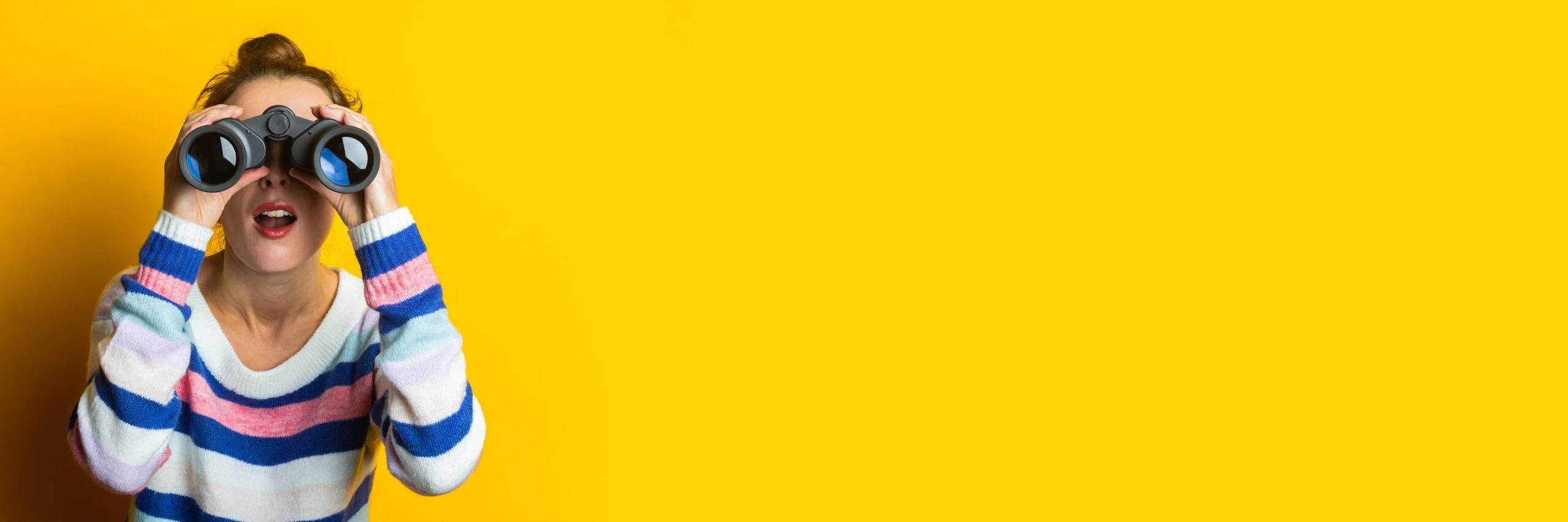 Enfant regardant à travers des jumelles sur un fond jaune.