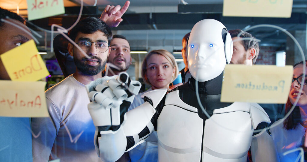 Un groupe de personnes se tient autour d'un robot humanoïde, qui écrit sur un tableau transparent couvert de notes autocollantes, capturant les émotions partagées au sein du groupe.